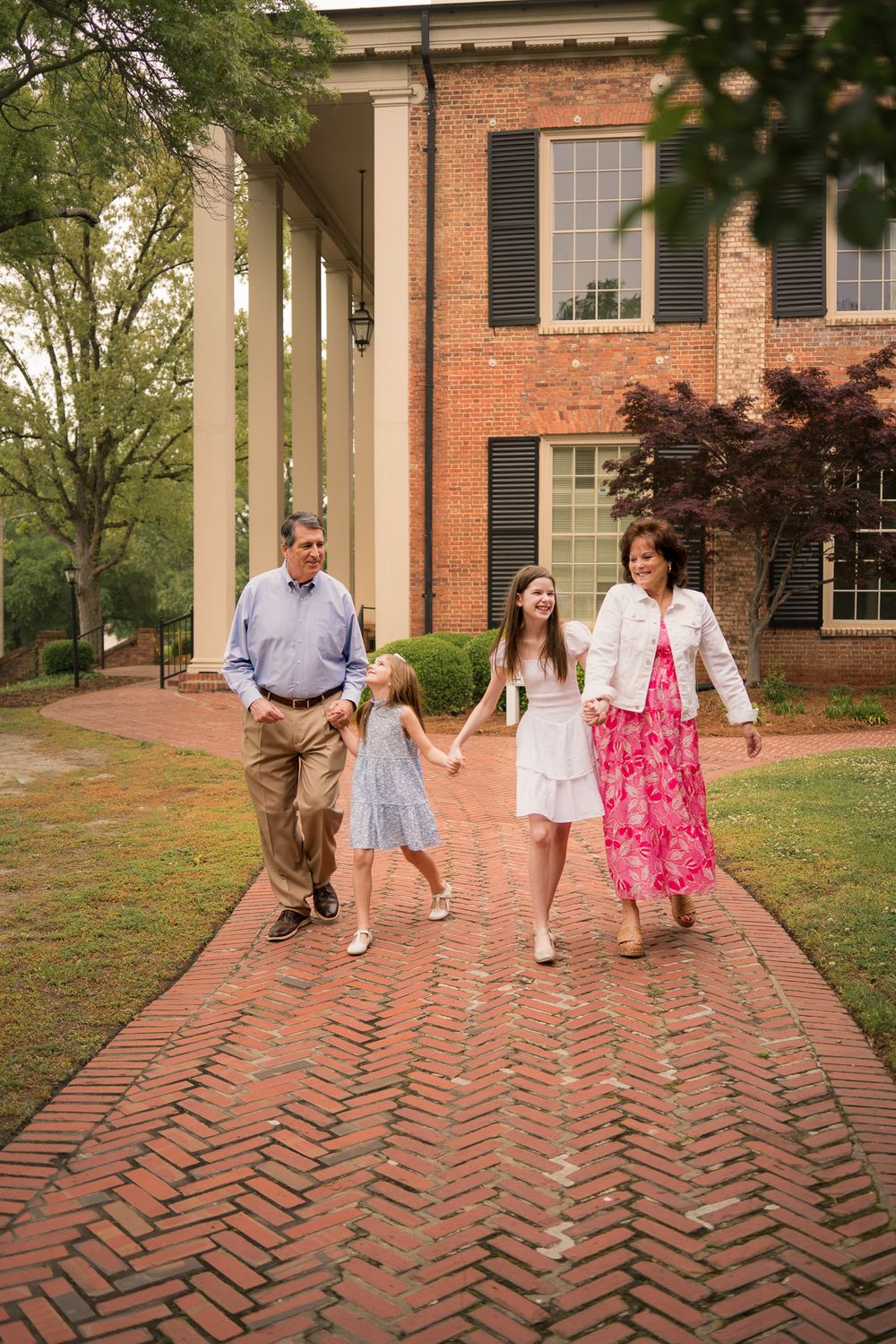 A family walks together on a brick pathway in front of a classic brick building with columns.