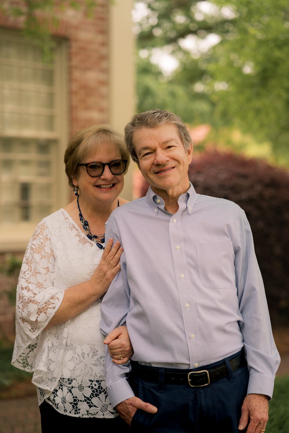 A couple shares a joyful moment together outdoors, with one wearing a white lace top and the other in a light blue shirt.
