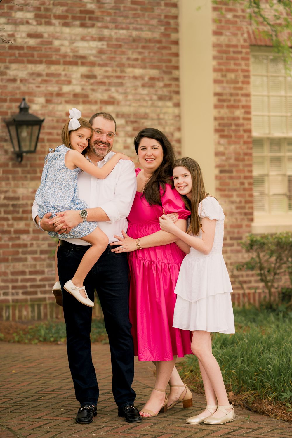A family shares joyful moments together against a brick wall backdrop in a series of candid outdoor portraits.