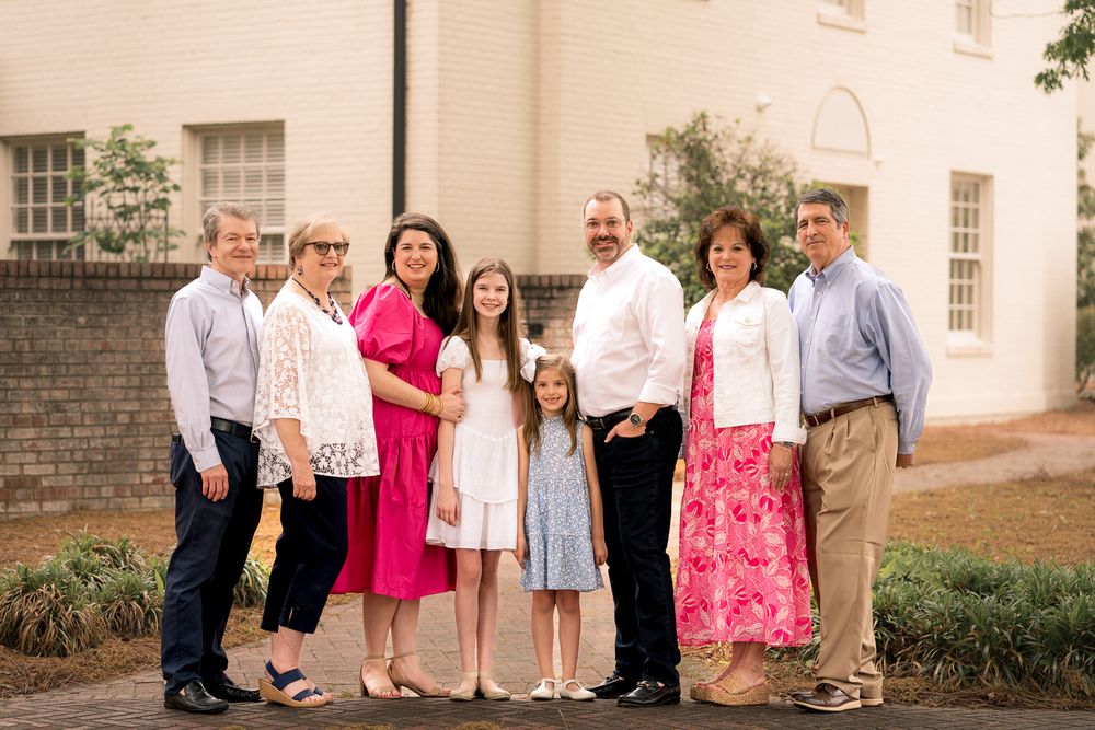 Family group portrait in pink and white outfits standing outside a brick building.