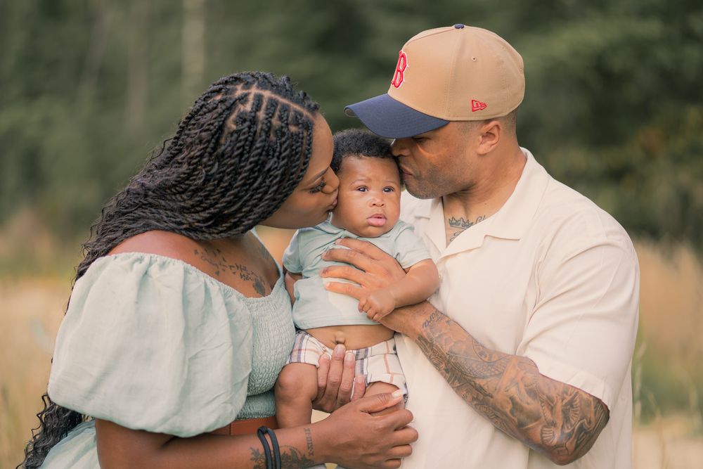 A tender family moment captured outdoors with a baby being held and embraced in a natural setting.