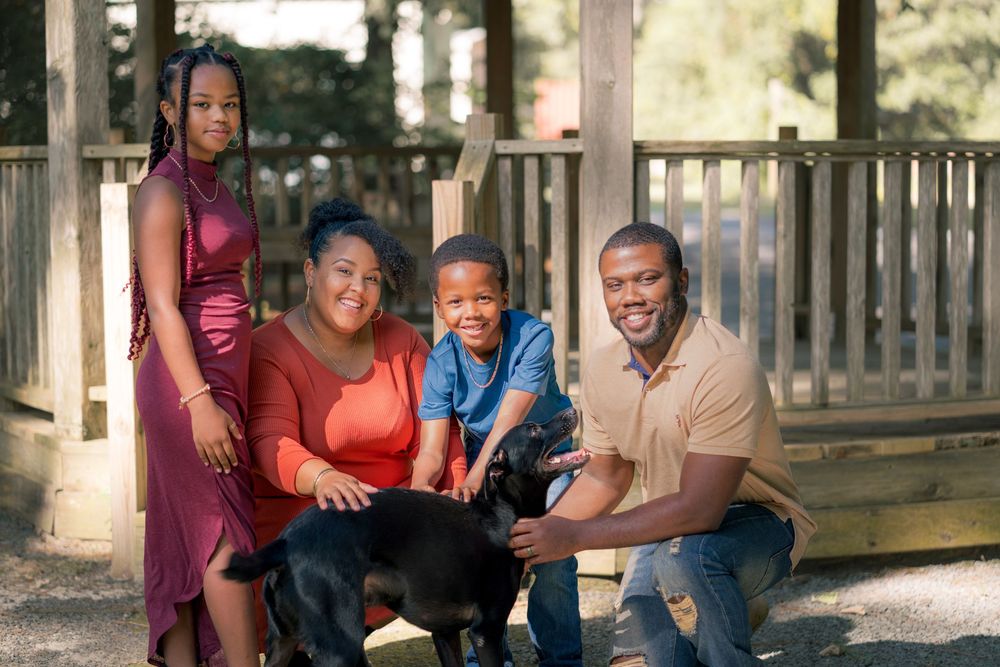 Family of four poses together on wooden deck during outdoor photoshoot.