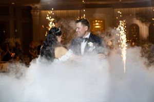 Bride and groom share first dance surrounded by dramatic fog and sparkling fireworks at elegant wedding reception.