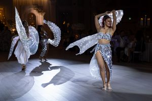 Dazzling performers in silver sequined costumes with wing accessories dance at upscale wedding reception entertainment.