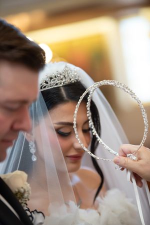 Bride wearing crystal tiara and veil during Orthodox wedding crowning ceremony with stefana crowns.