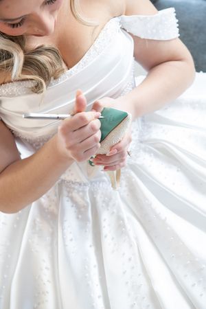 Bride in white wedding gown writing on the sole of her gold wedding shoe before the ceremony.