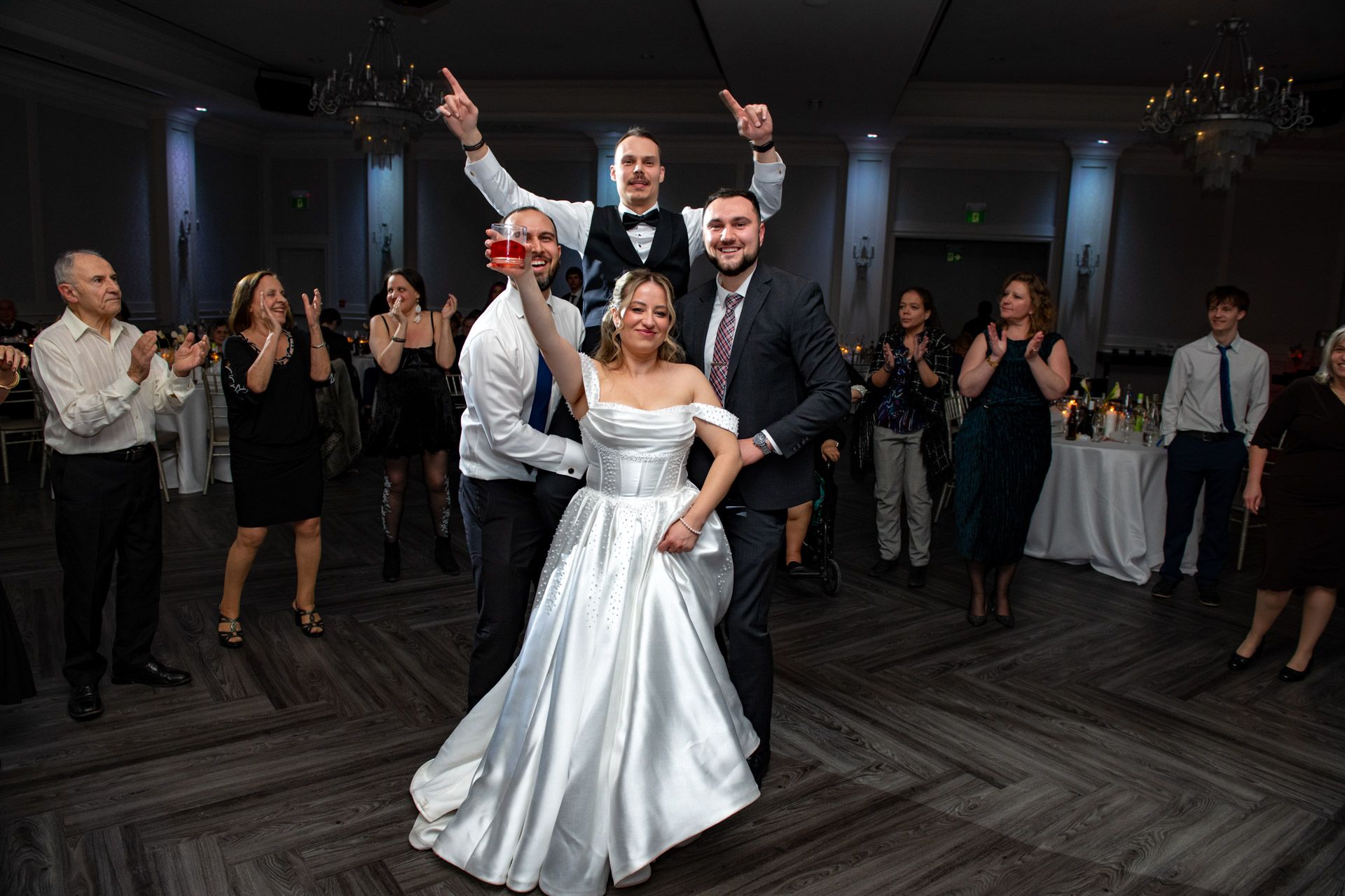 Joyful wedding reception dance floor moment with bride, groom and guests celebrating together.