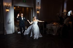 Bride and groom making a grand entrance into elegant wedding reception ballroom wearing sunglasses.
