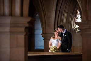Bride and groom share an intimate kiss framed by Gothic stone arches in a historic church.