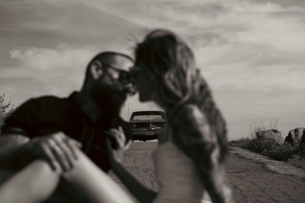 A blurry black and white artistic photograph showing motion on a dirt road with a car in the background.