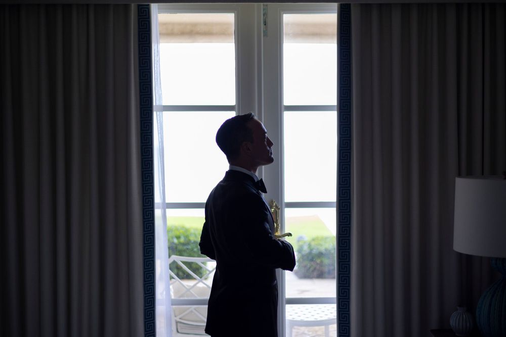 Silhouette of person in suit standing by window in room with curtains and natural lighting.