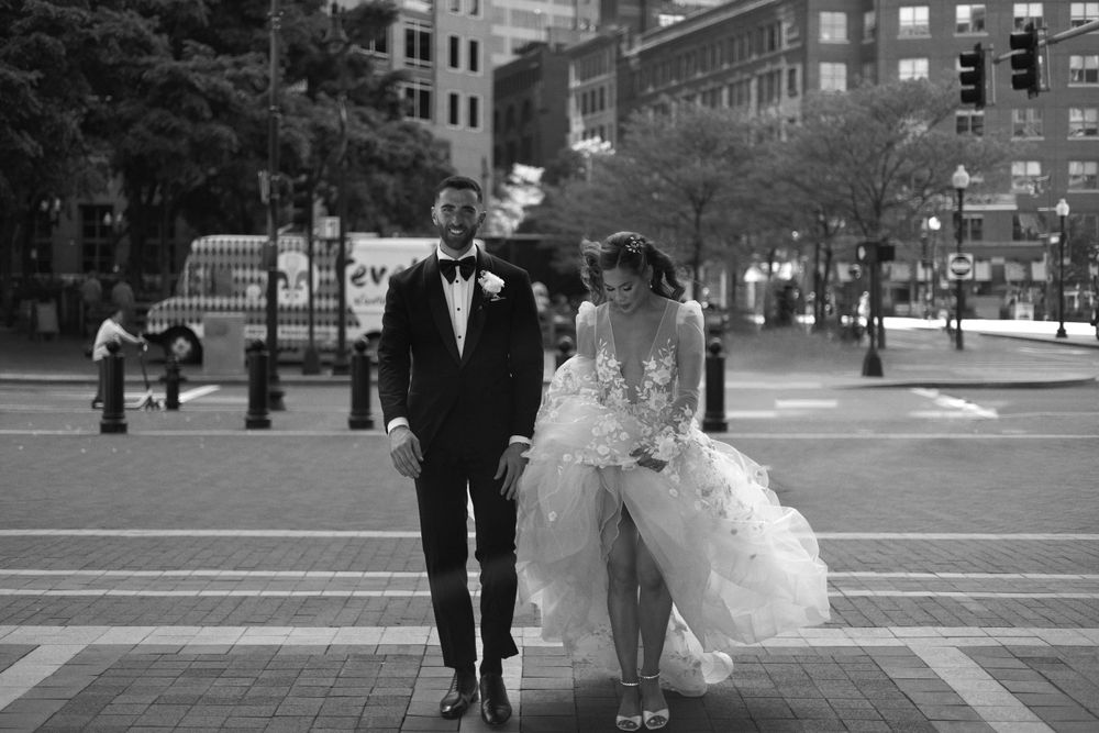 A bride and groom share a romantic moment walking together on a city street in black and white photography.