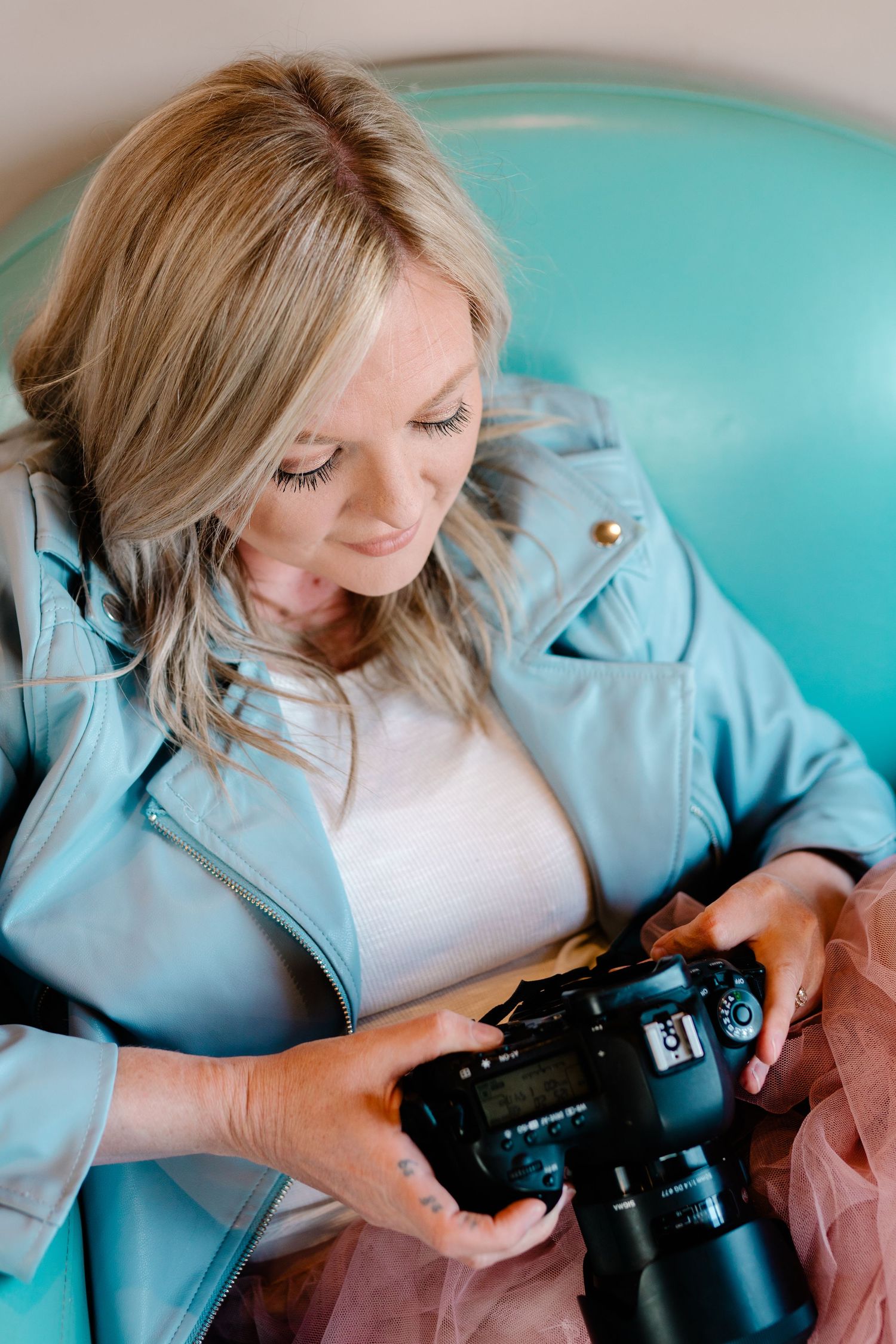 Photographer in light blue leather jacket reviewing images on professional camera.