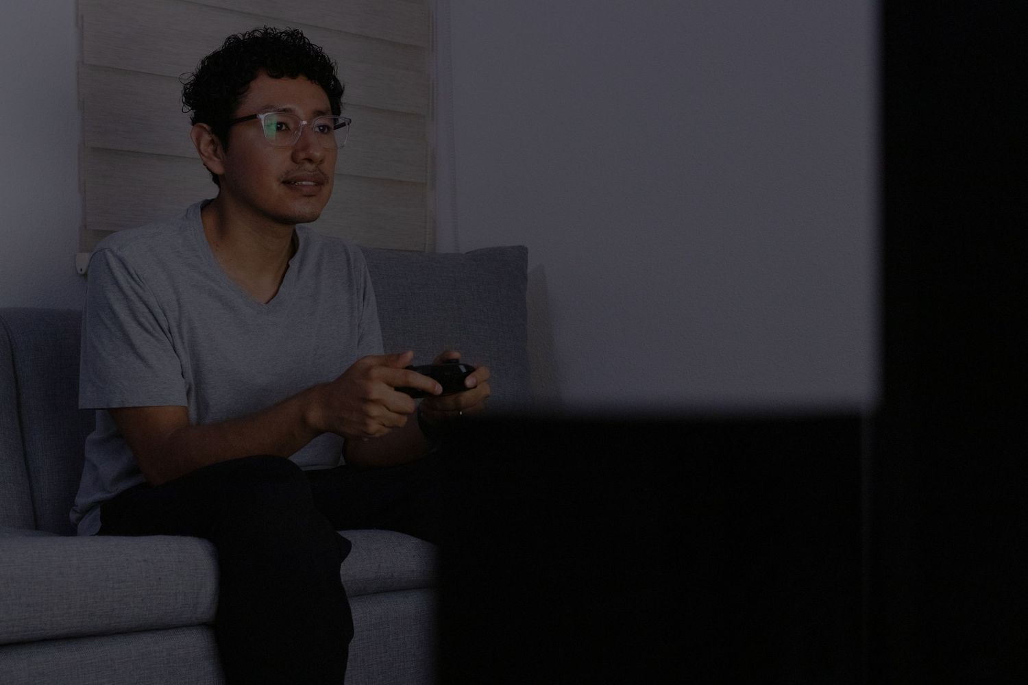 Figure wearing glasses illuminated by screen light in dark setting.