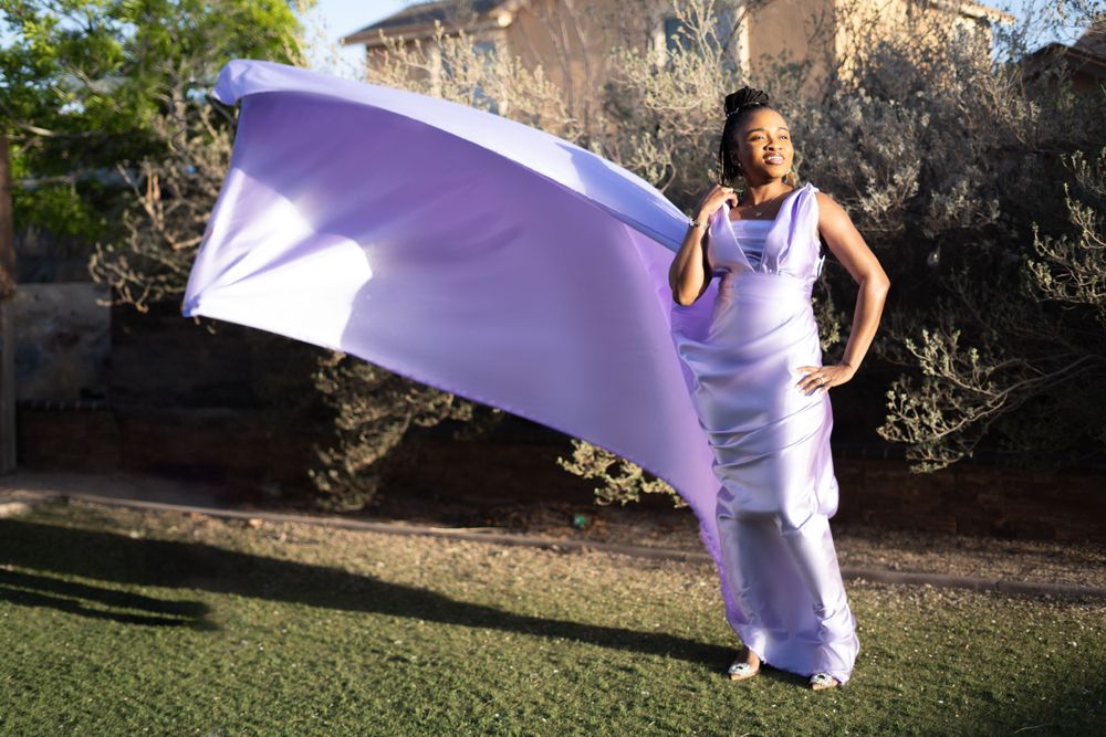 Person in lilac dress stands on grass as fabric flows dramatically in the breeze.
