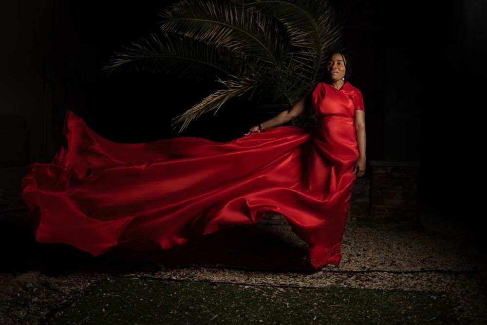 Dramatic portrait with flowing red dress billowing against dark background with palm tree silhouette.