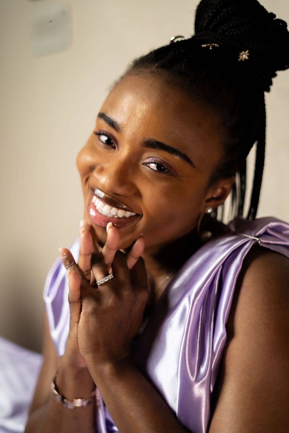 Person in purple silk showing joyful expression while touching their face with rings.