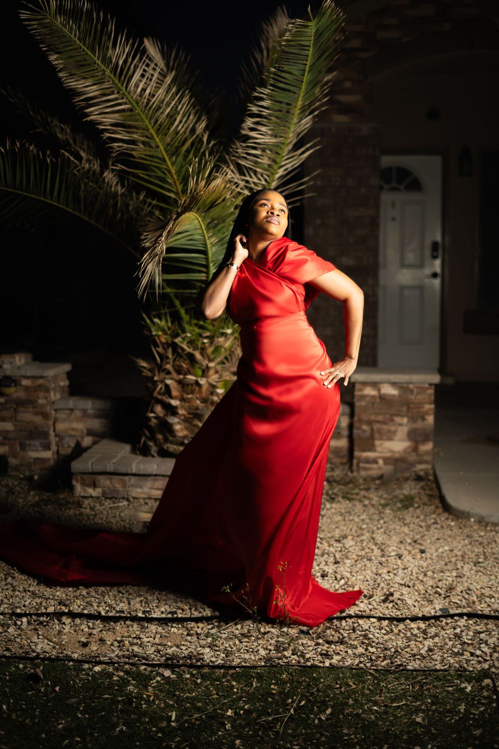 Dramatic nighttime portrait with red flowing gown against palm fronds backdrop.