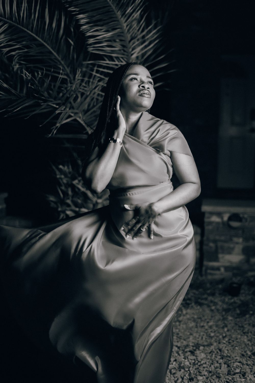 Artistic black and white portrait of person in silk dress against palm leaves.