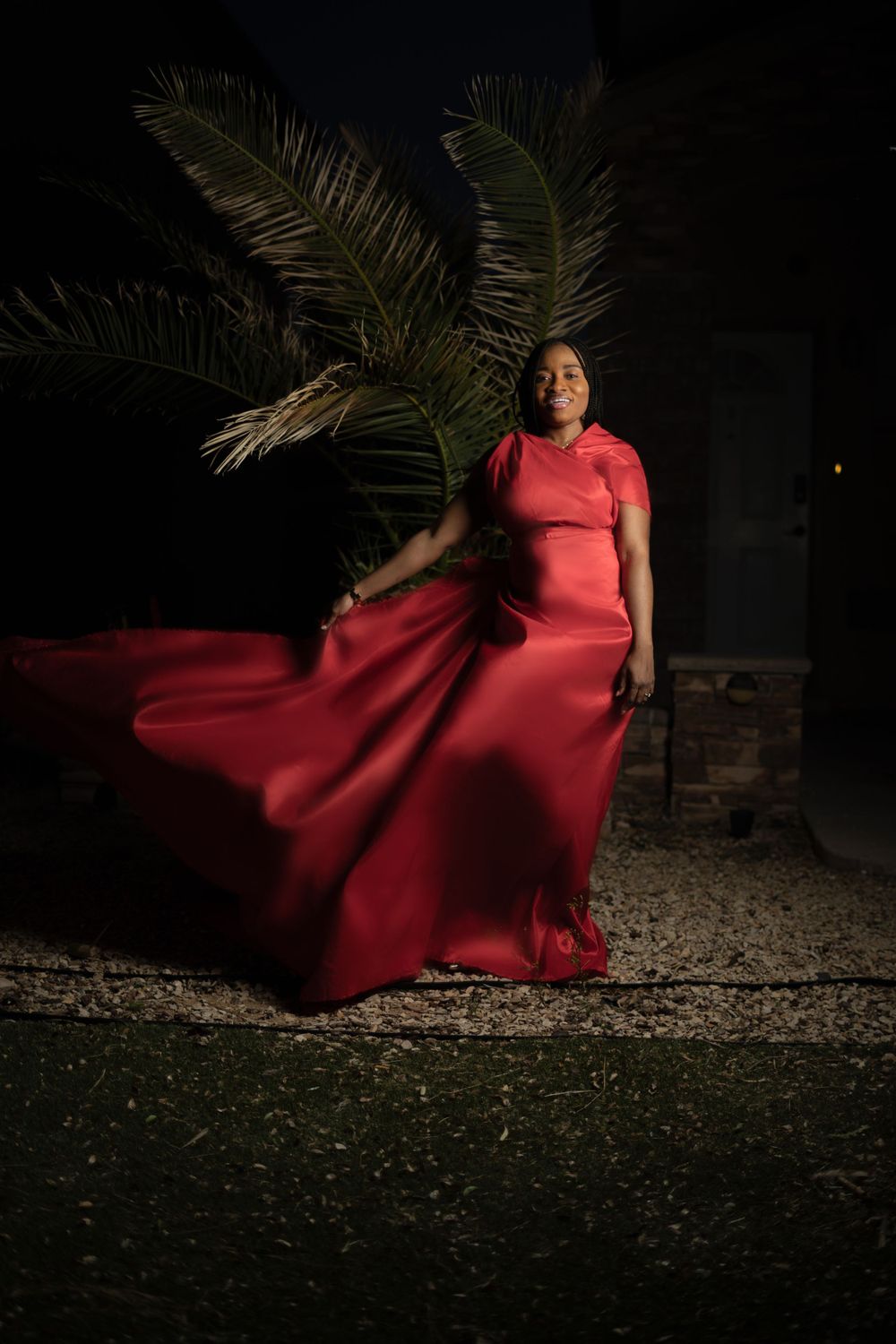 Dramatic fashion shot of flowing red dress catching wind against palm trees at night.