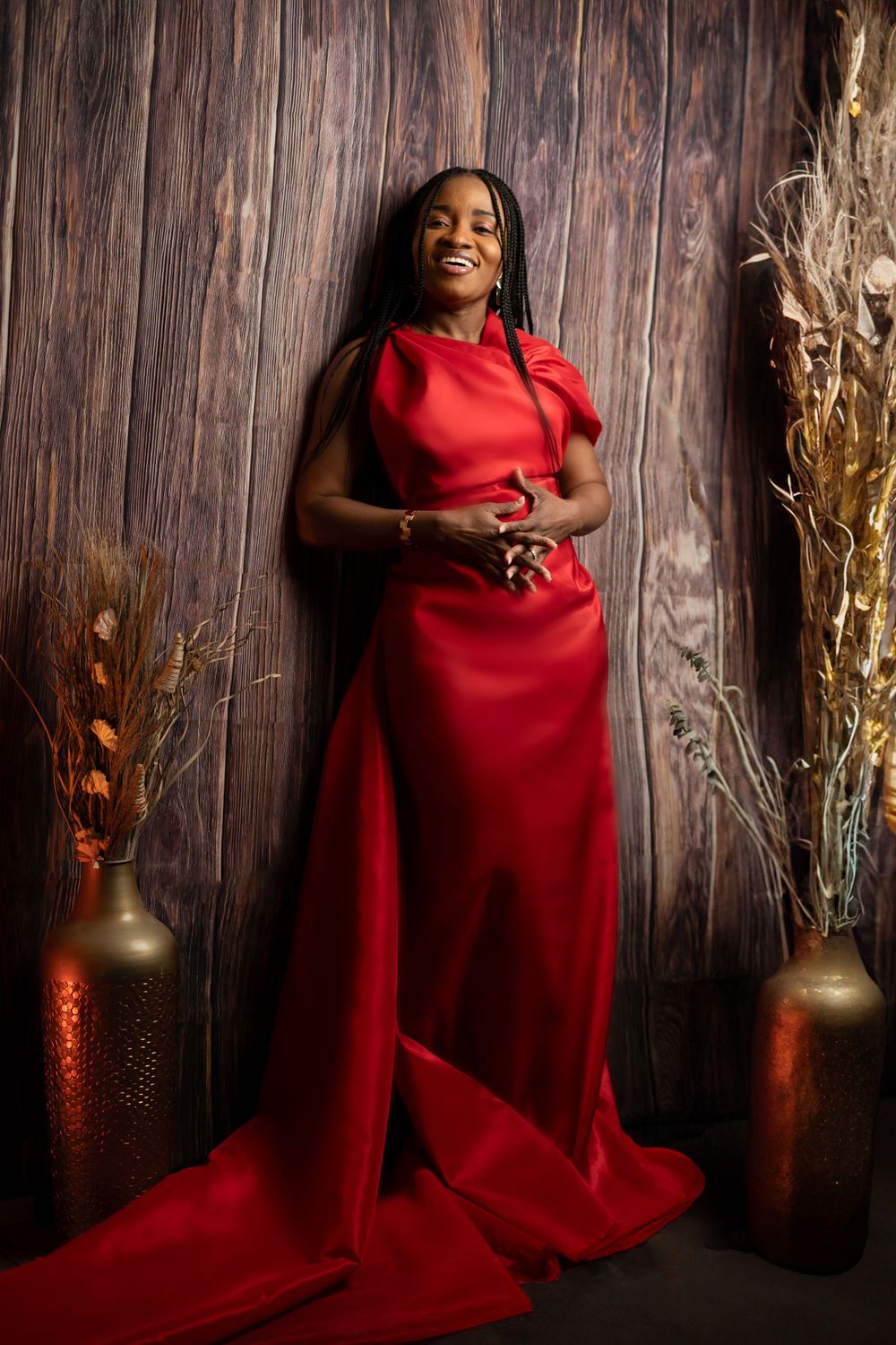 Artistic portrait session with person in red gown against rustic wooden wall with decorative elements.