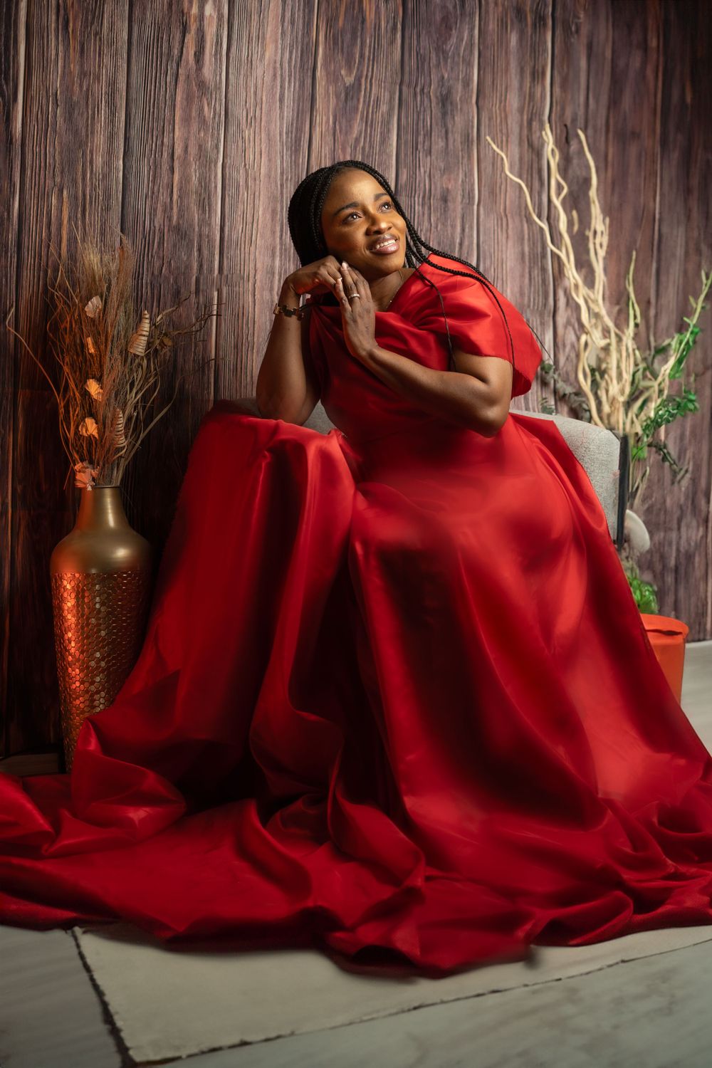 Person in flowing red dress lounging gracefully against rustic wooden background with decorative vases.