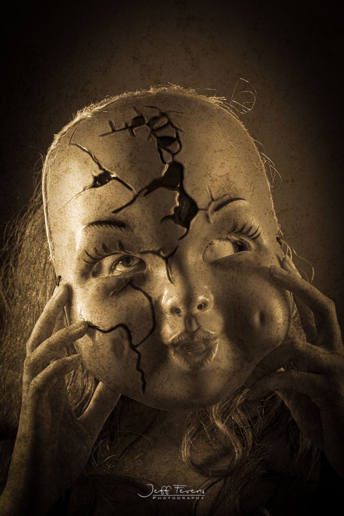 A Sepia tones images of a woman holding a cracked porcelain doll mask infant of her face.