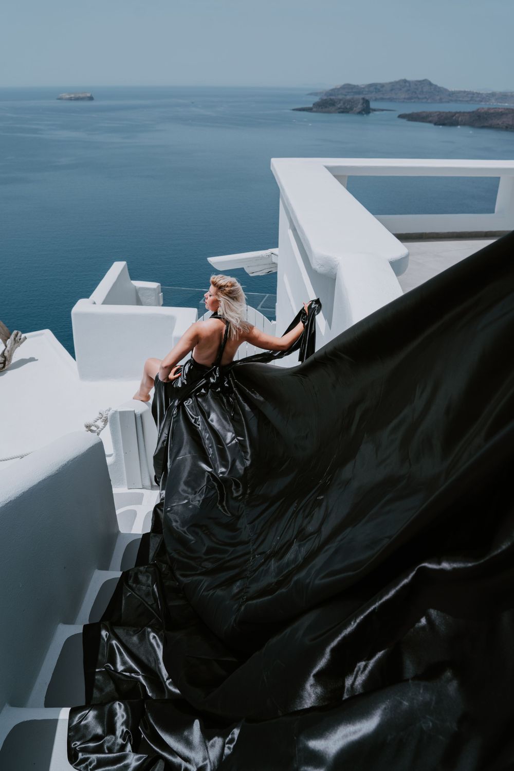 Dramatic black fabric flows against white Santorini architecture overlooking the Mediterranean.