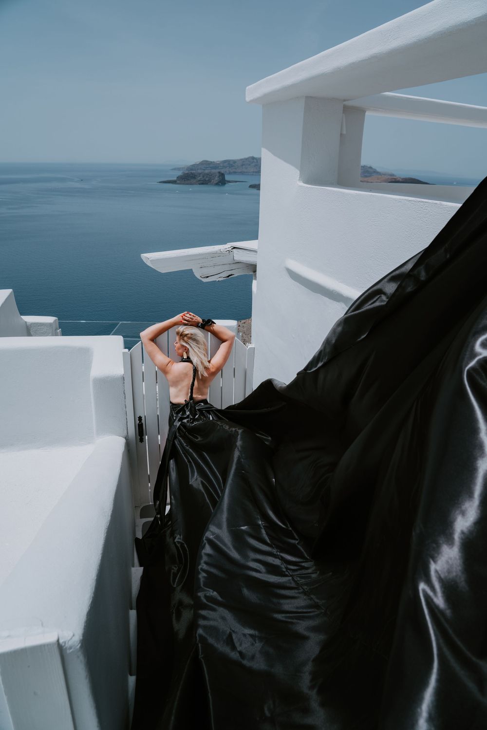 Black flowing fabric creates contrast against white buildings and blue ocean views in Greece.