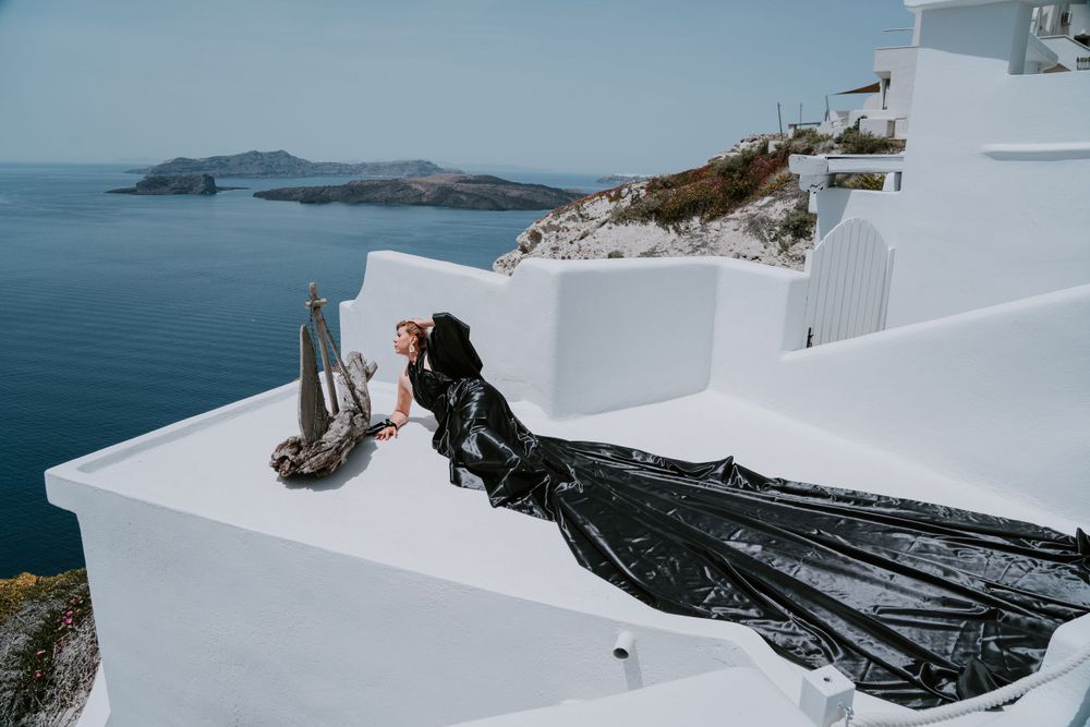 A flowing black dress against white architecture overlooking the Santorini caldera in Greece.