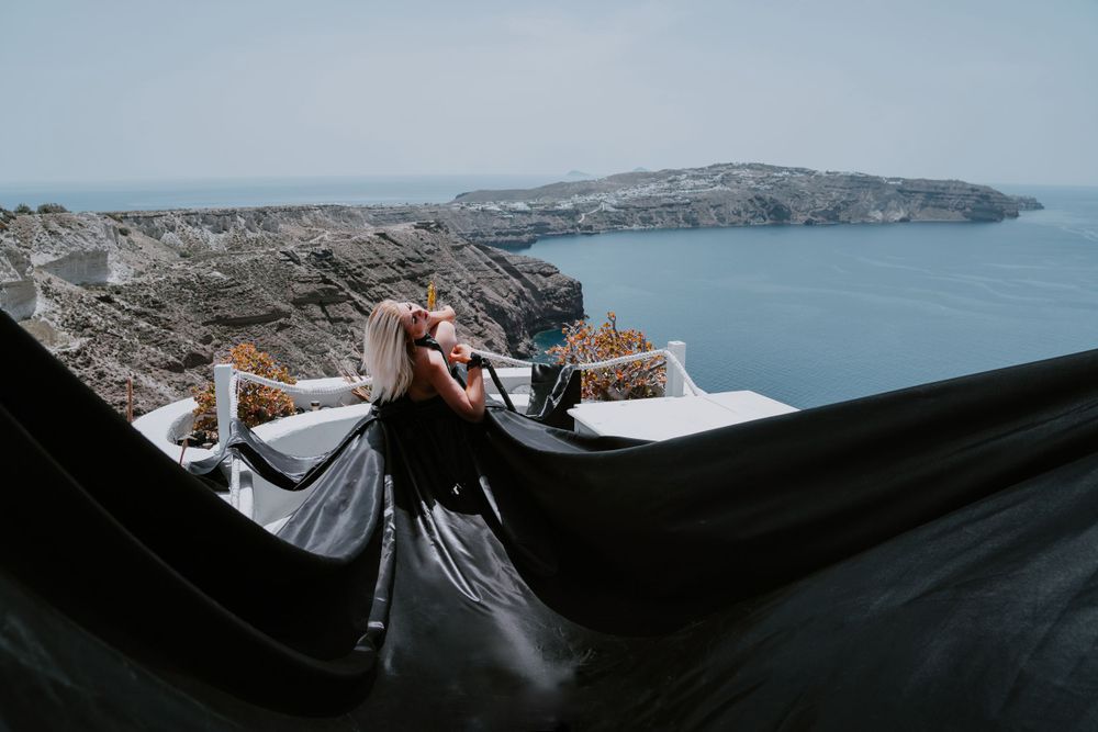 Dramatic black fabric billows against whitewashed architecture with ocean views in Santorini.