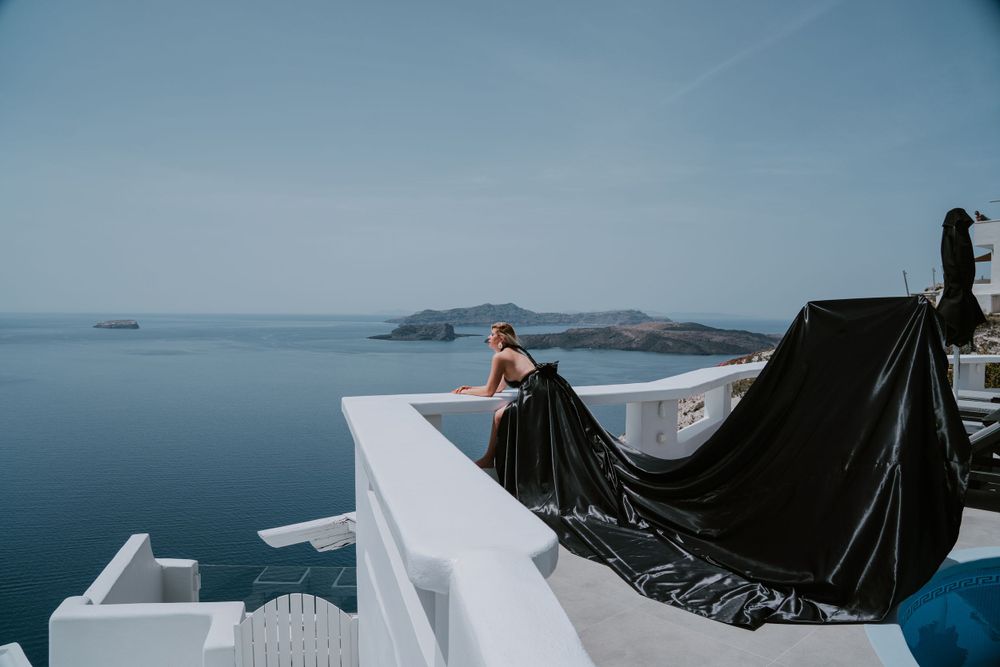 Long black dress flowing in the wind against classic white Greek island architecture.