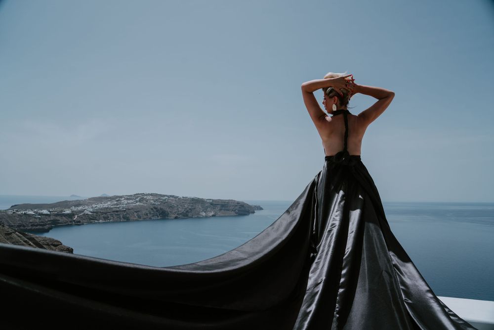 Silhouette posing with flowing black fabric against coastal Mediterranean backdrop.