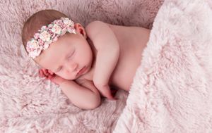 Peaceful newborn wearing floral headband sleeping on pink fur backdrop.