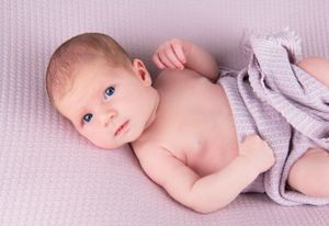 Baby lying on purple textured blanket wearing grey wrap.