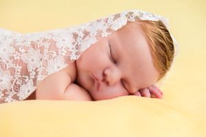 Peaceful sleeping infant wrapped in delicate white lace against soft yellow background.