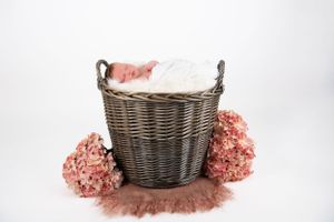 Sleeping newborn nestled in dark woven basket with pink floral accents.