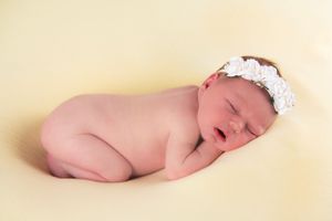 Sleeping newborn with white headband on cream colored backdrop.