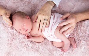 Professional newborn photography session with hands gently supporting baby.