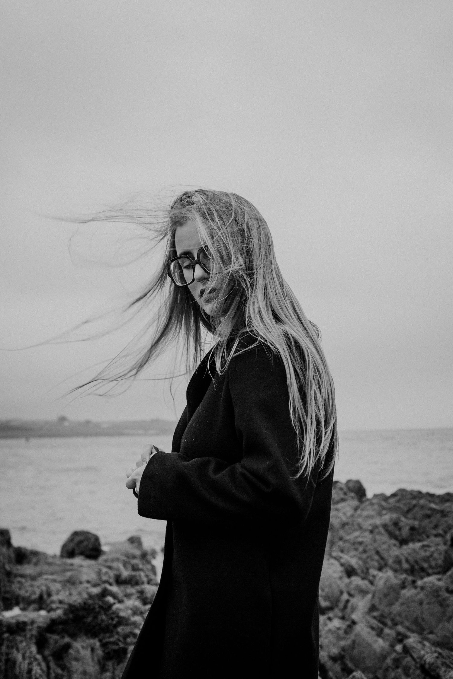 Dramatic black and white photo of wind-swept hair against coastal background.