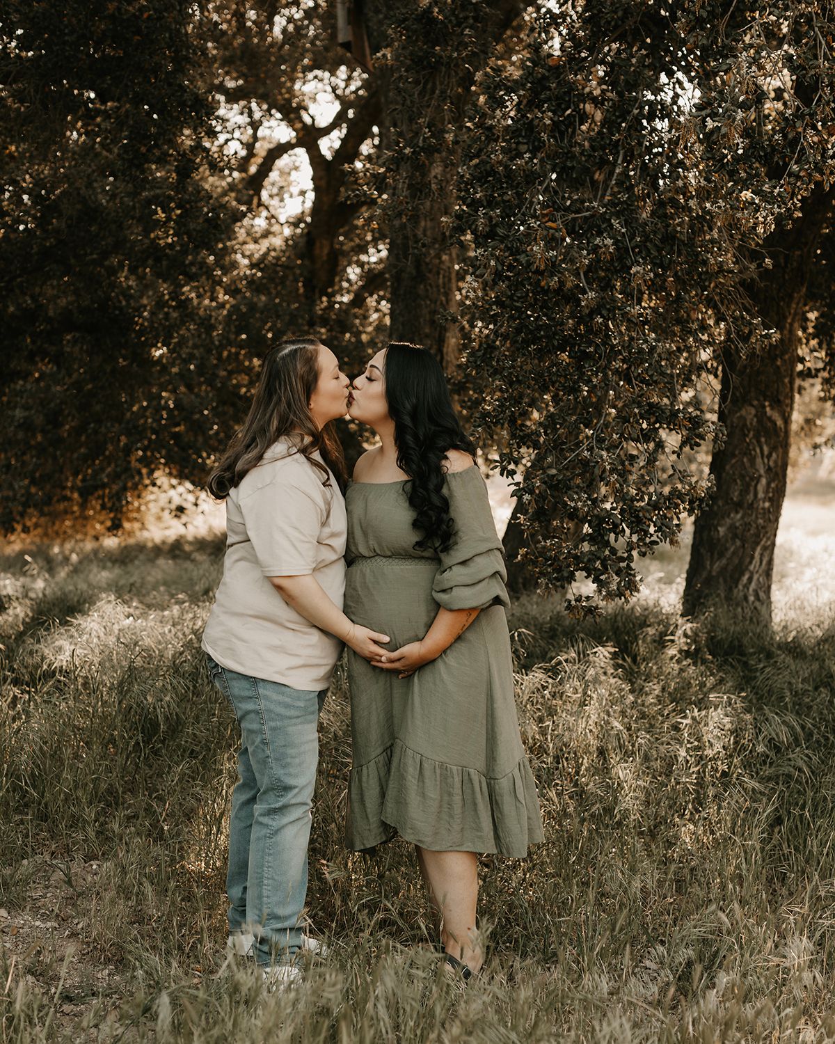 Two people in casual attire interact playfully in a sunlit meadow under oak trees.