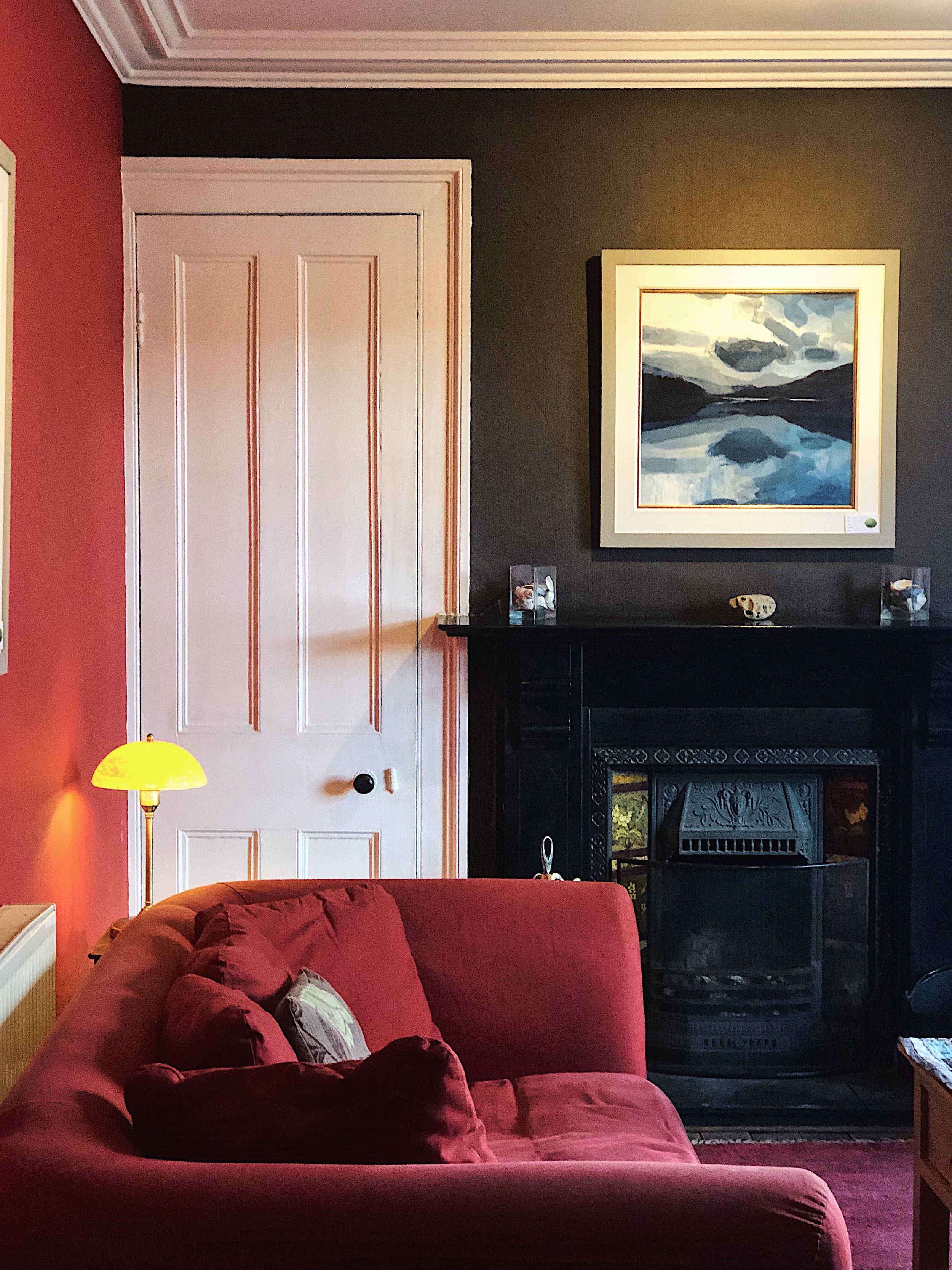 Cozy living room interior with red walls, plush burgundy sofa, and framed artwork captured at different times of day.