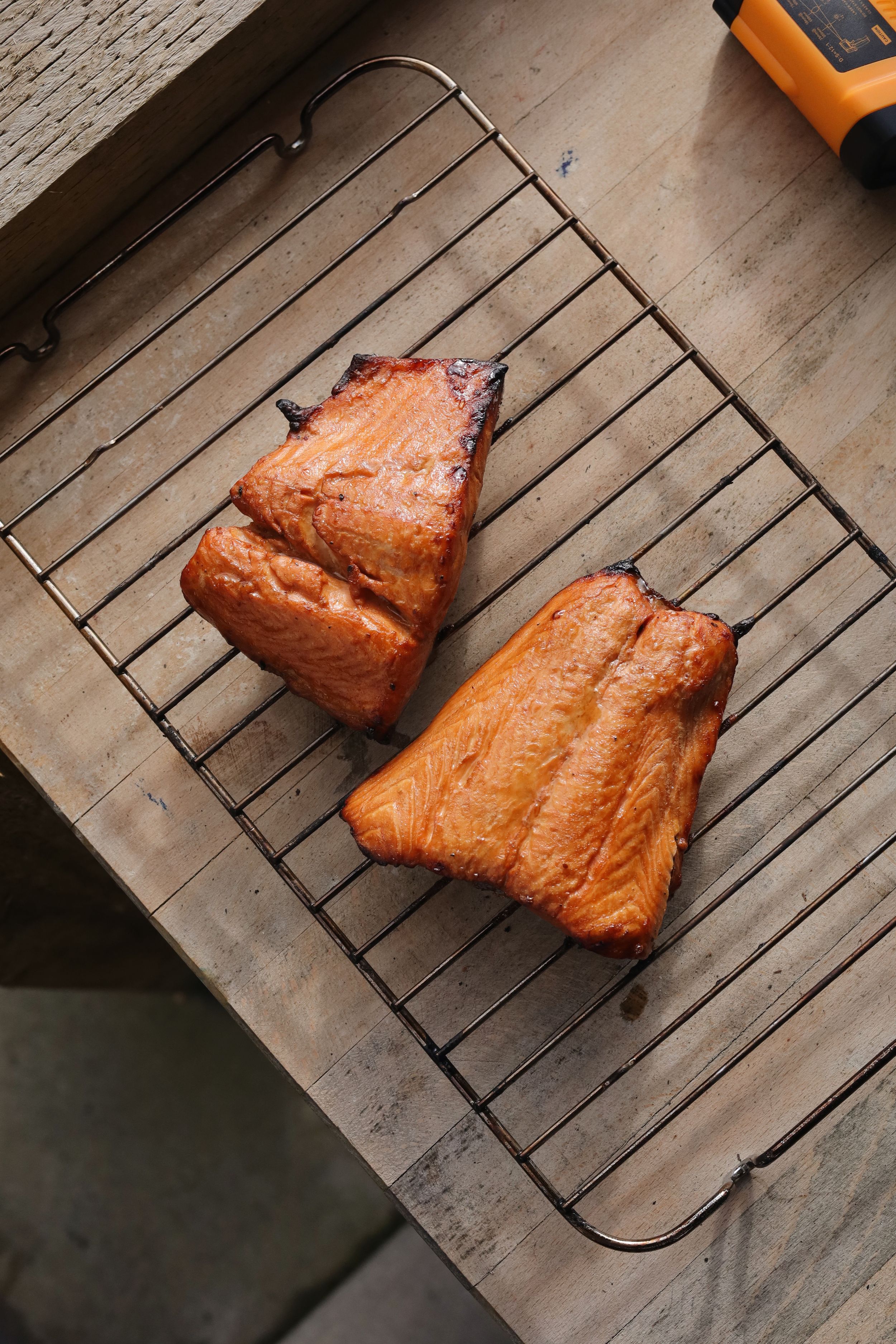 Grilled salmon fillets resting on a wooden cooling rack showing various stages of cooking.