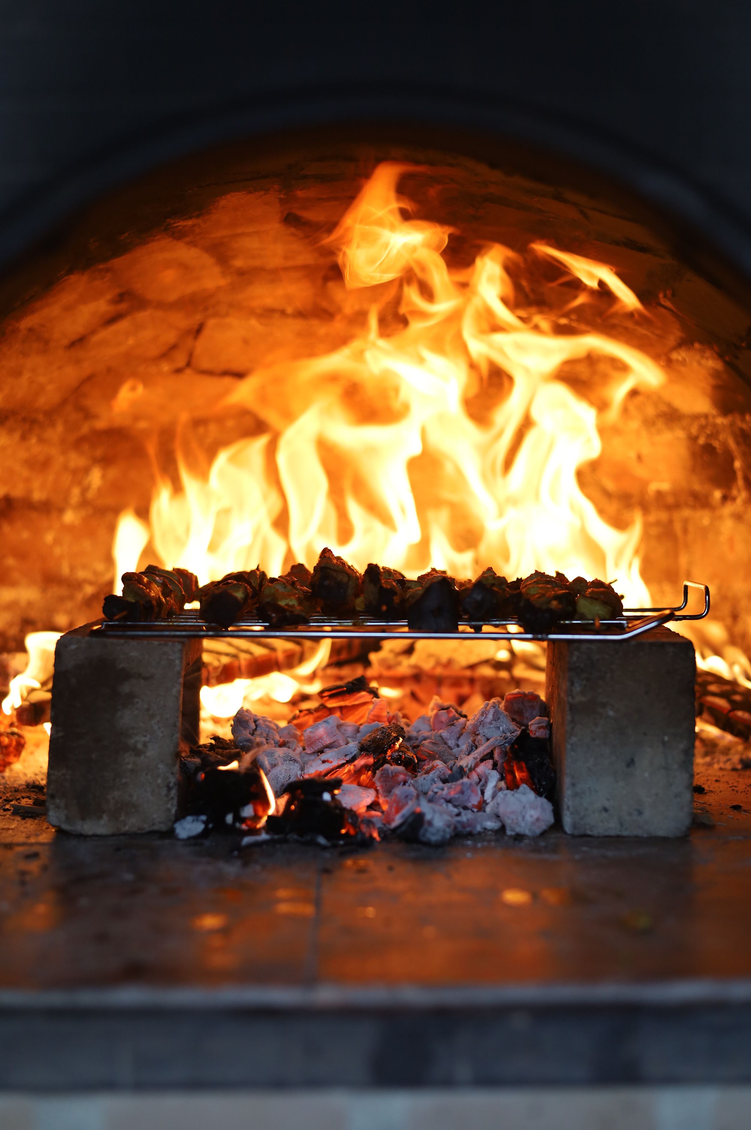 Wood-fired pizza oven with bright orange flames and glowing embers shown in sequential shots.