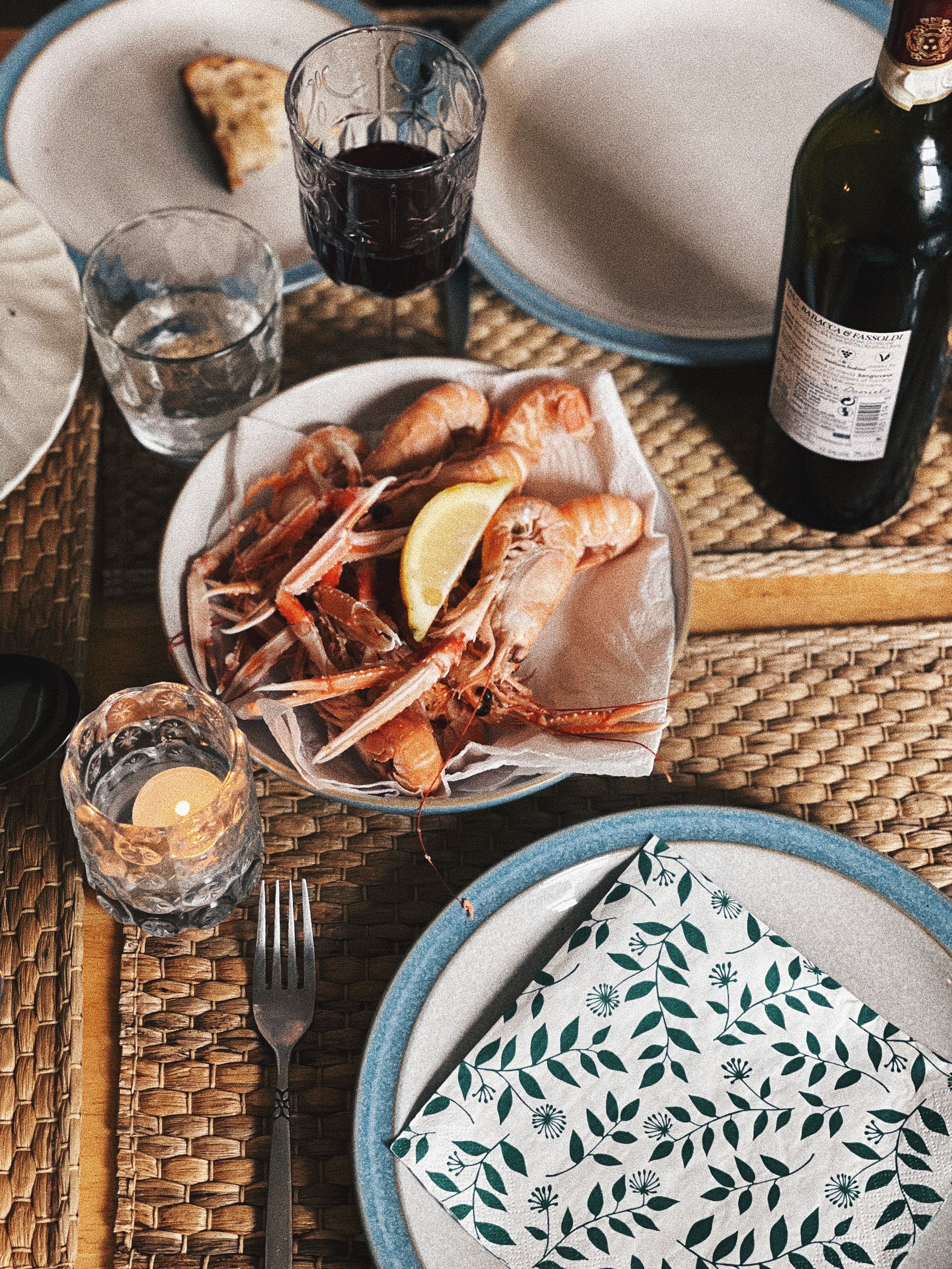Elegant table setting with patterned plates, wine glasses, and seafood on a woven placemat.