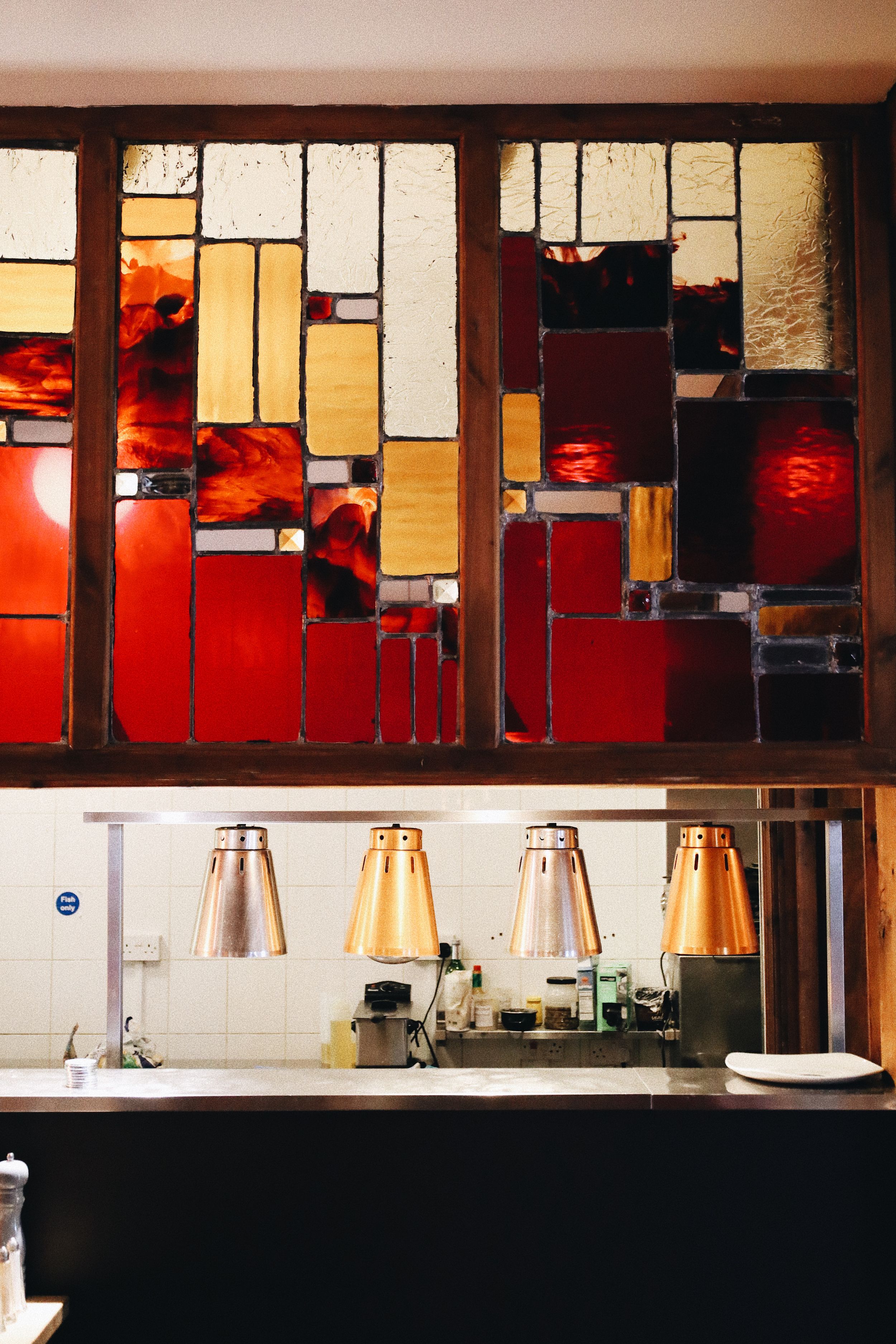 Modern restaurant interior with geometric stained glass panels and industrial pendant lighting.