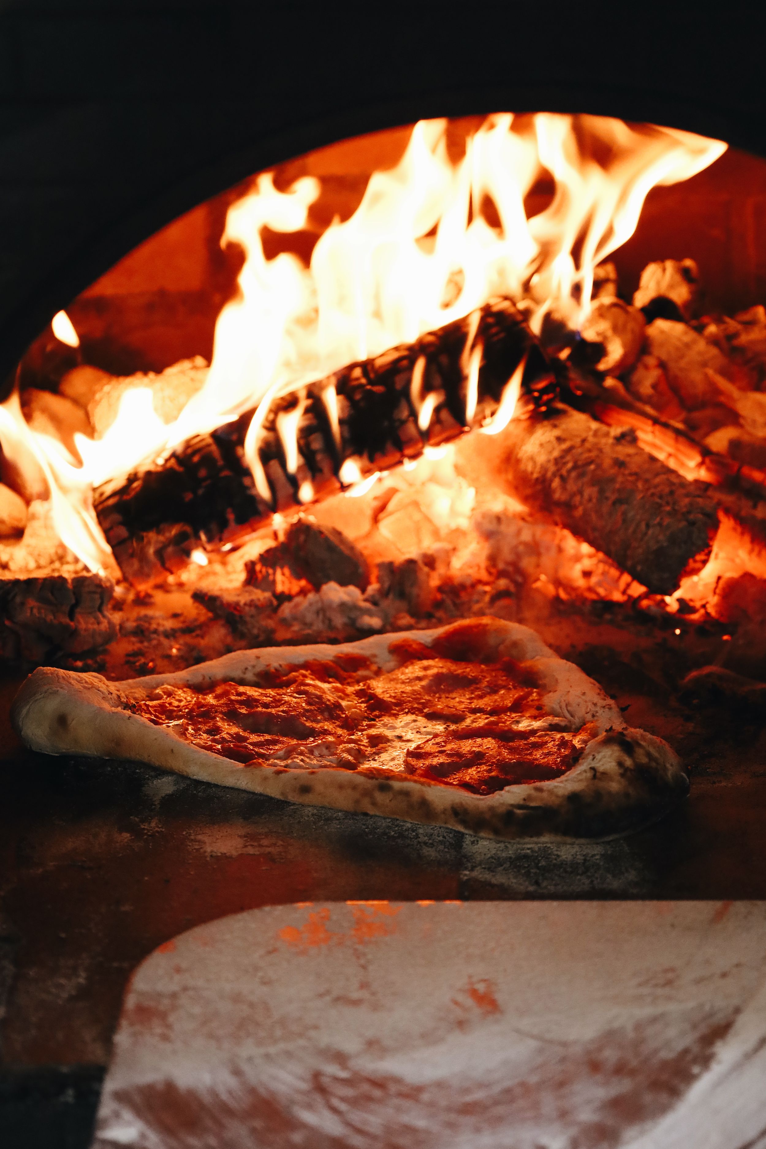 Pizza baking in a fiery wood-burning oven showing various stages of cooking.
