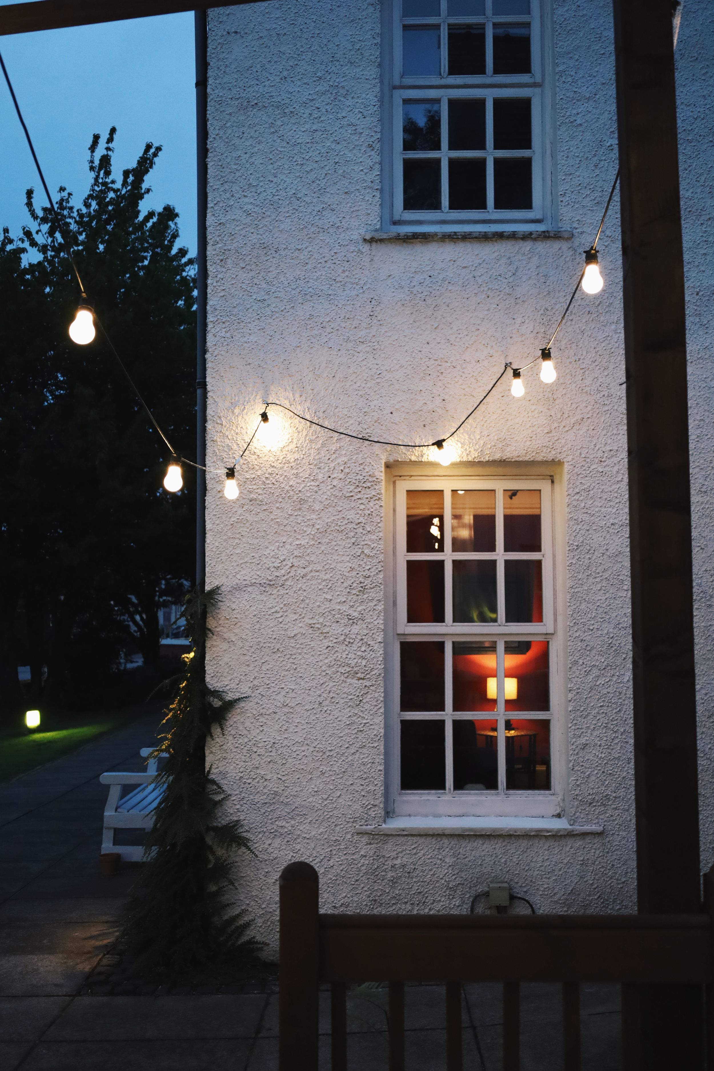 White house exterior at dusk with string lights creating a warm ambiance.