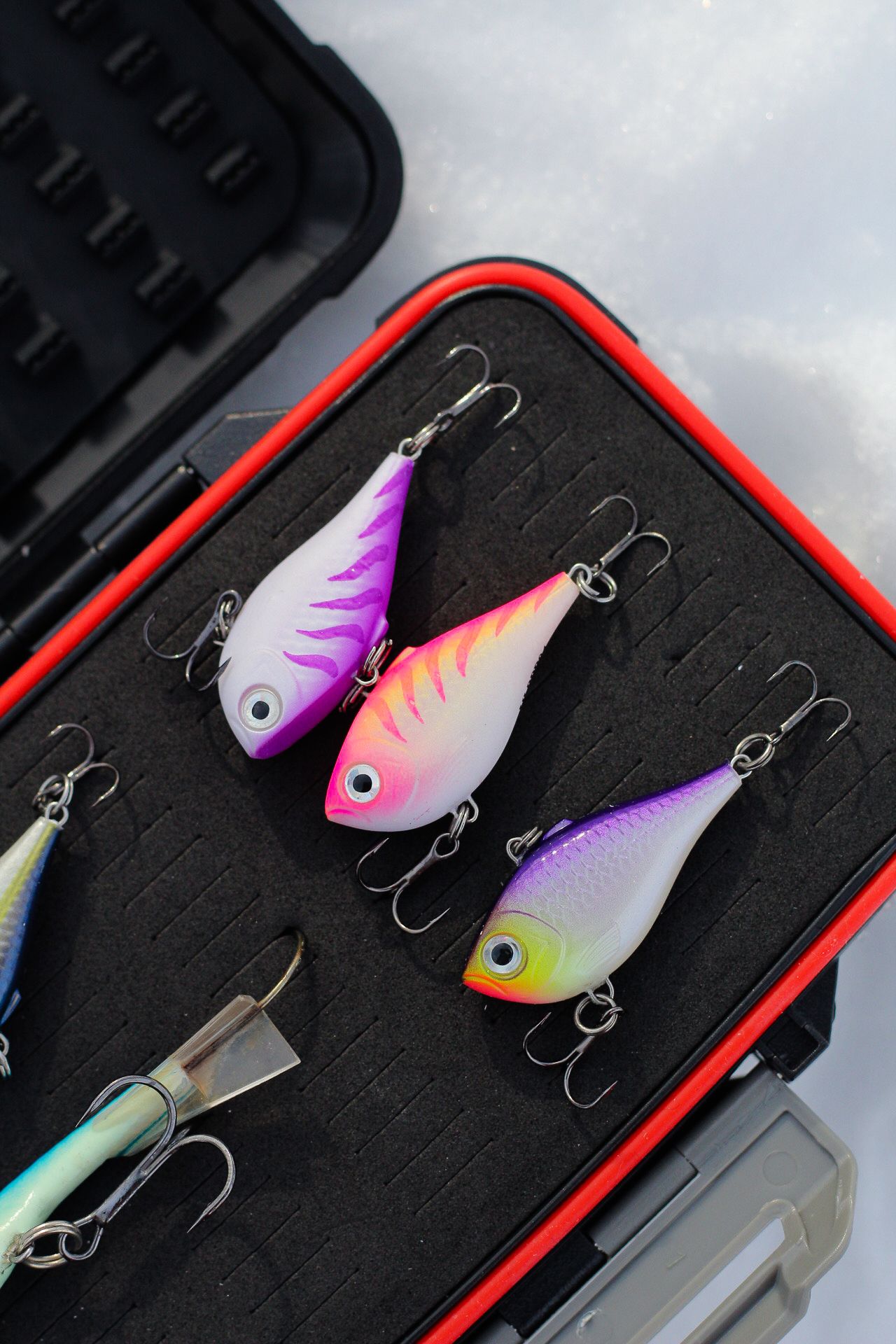 Colorful fishing lures displayed in a black and red tackle box.