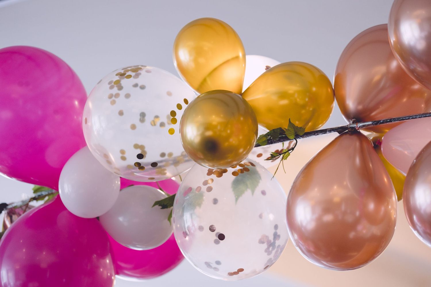 Colorful party balloons in pink, gold, and rose gold with confetti-filled transparent ones arranged in a cluster.